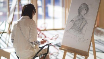A person drawing on paper in front of an easel