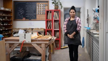 Naomi Hobson standing next to a wooden table and metal sink in her studio