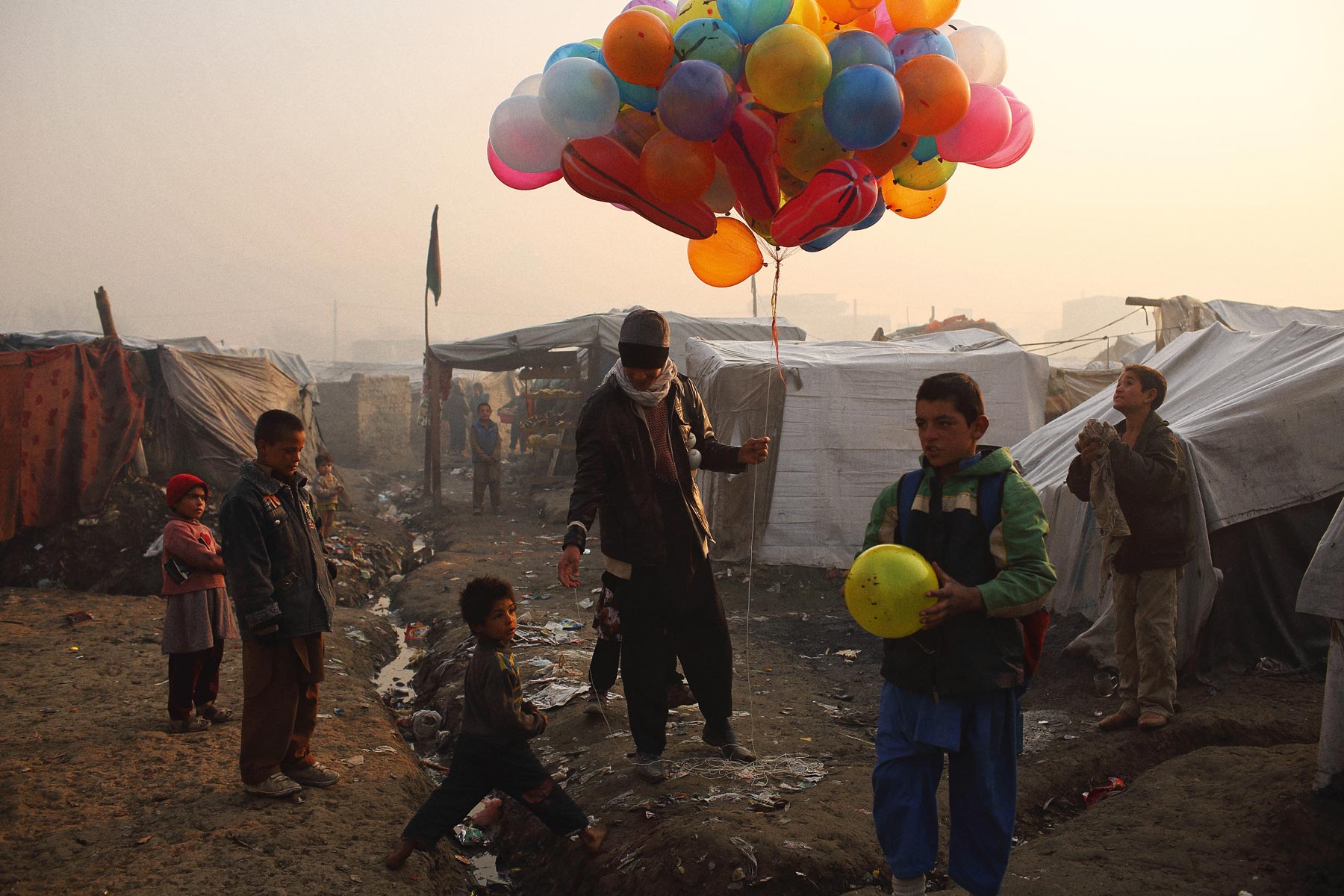 At sunrise, a balloon seller makes his way through an informal settlement for families displaced by fighting in Afghanistan’s provinces, beside Kabul’s national cricket stadium, 2014 Andrew Quilty