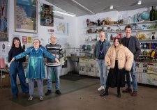 Two grounps of three people standing in a studio with walls and shelves filled with artworks