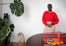 Atong Atem standing behind a wooden table and next to a large leafy green plant