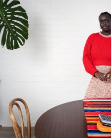 Atong Atem standing behind a wooden table and next to a large leafy green plant