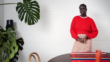 Atong Atem standing behind a wooden table and next to a large leafy green plant