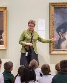 A teacher with a group of children in front of a painting in a gallery