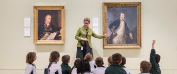 A teacher with a group of children in front of a painting in a gallery