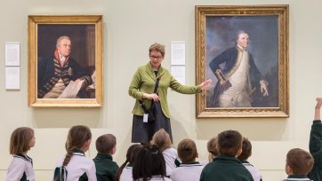 A teacher with a group of children in front of a painting in a gallery