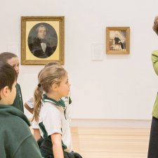 A teacher with a group of children in front of a painting in a gallery