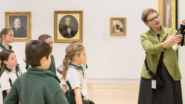 A teacher with a group of children in front of a painting in a gallery