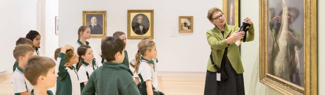 A teacher with a group of children in front of a painting in a gallery