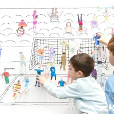Children placing paper cutouts of athletes on a soccer wall scene