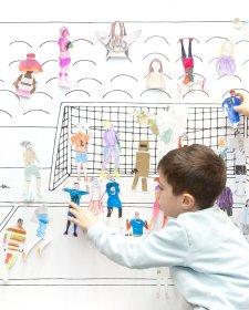 Children placing paper cutouts of athletes on a soccer wall scene