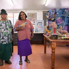 Dulcie Sharpe and Rhonda Sharpe in a room with a brown tile floor, next to a wooden table with soft animal sculptures