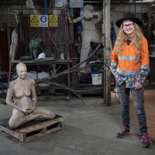 Nell standing in her workshop next to a cross legged sculpture