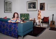 Deborah Kelly sitting on a blue couch in a room with artworks on the walls
