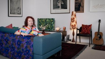 Deborah Kelly sitting on a blue couch in a room with artworks on the walls