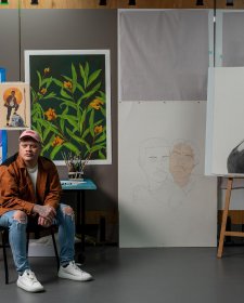 Dylan Mooney sitting on a chair in front of a wall with paintings and drawings