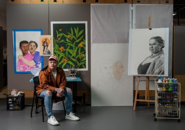 Dylan Mooney sitting on a chair in front of a wall with paintings and drawings